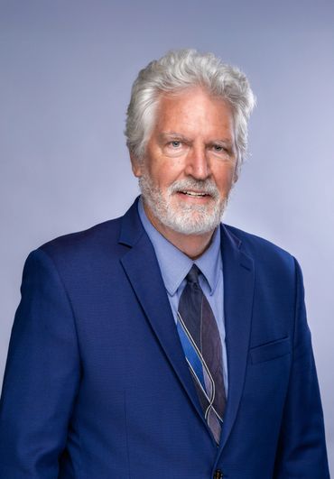 Older man with white hair and beard in a blue suit and tie.
