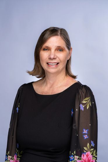 Smiling woman with shoulder-length brown hair in a black dress with floral sleeves.