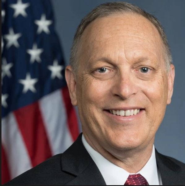 Smiling man in suit with American flag background.