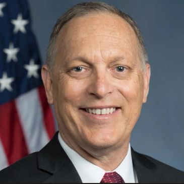 Smiling man in suit with American flag background.