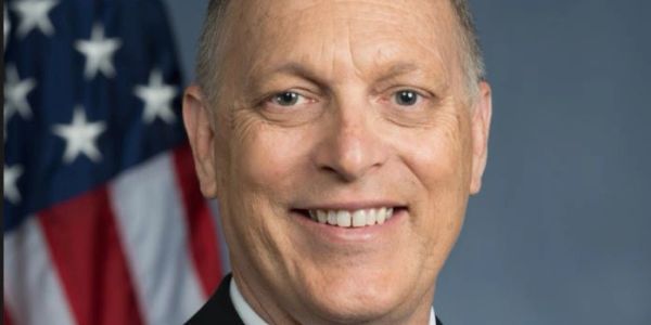 Smiling man in suit with American flag background.