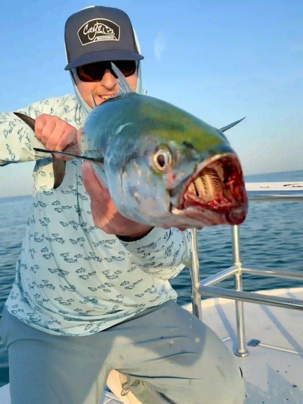 Man holding a large fish on a boat under clear blue sky on a clearwater fishing charter