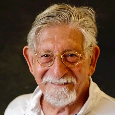 Smiling elderly man with white hair and glasses.