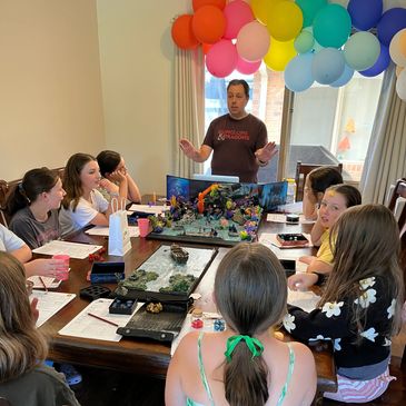 Group playing Dungeons & Dragons around a table with colorful balloons overhead.