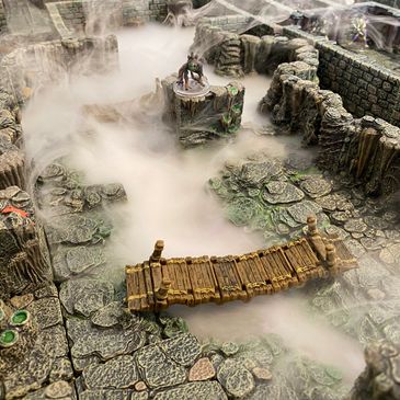 A fog-filled dungeon scene with a wooden bridge and fantasy miniatures.