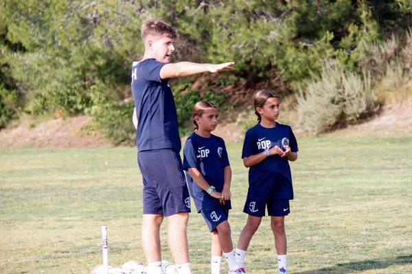 Coach instructing two kids on a soccer field.
