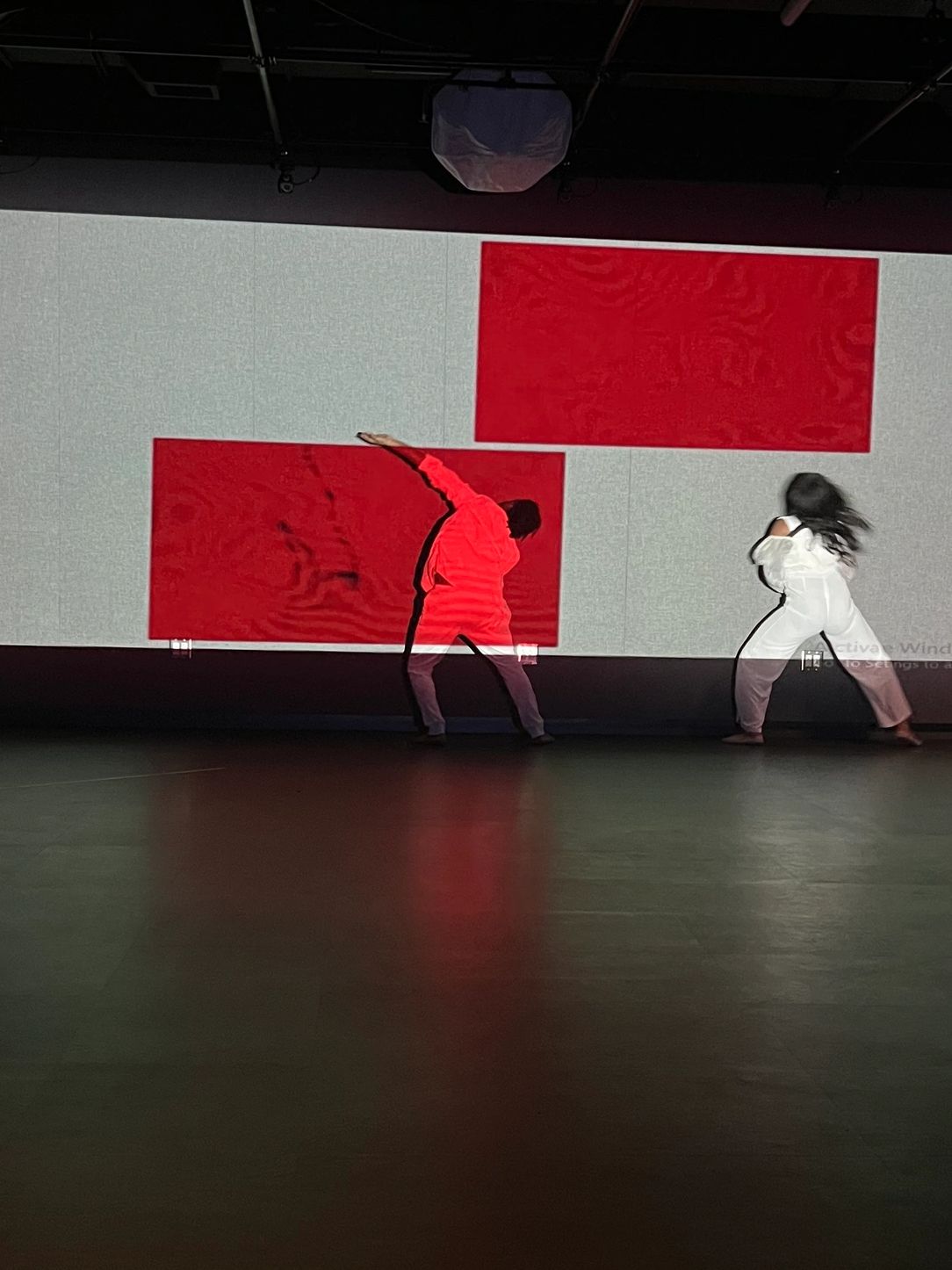 Three performers in a dark room with red and white projections on the wall.