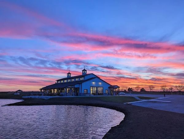 A large building by a pond during a colorful sunset.