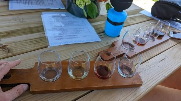 Two wooden flight paddles with small glasses containing different colored drinks on a wooden table.