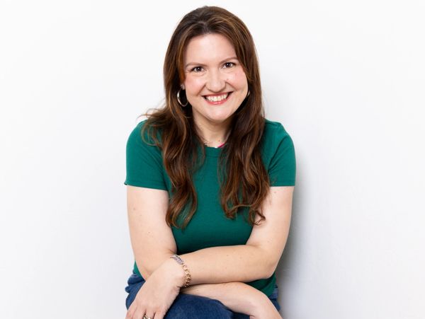 Smiling woman in a green shirt sitting against a white wall.