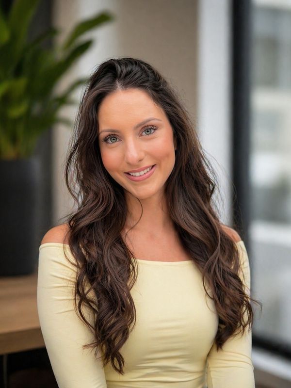 Smiling woman with long brown hair wearing an off-shoulder cream top.