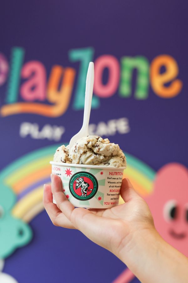 Hand holding ice cream cup with a spoon against colorful background.