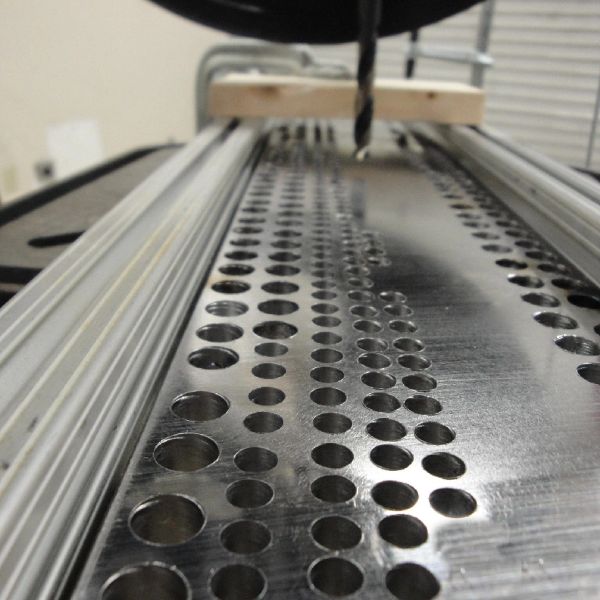 Close-up of metal sheet with drilled holes and a drill bit.