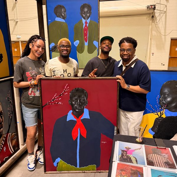 Four people proudly display vibrant, expressive paintings of young Black boys in formal attire.