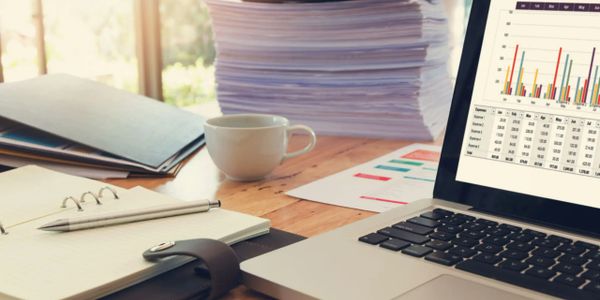 Workspace with laptop showing expense trends, paperwork, and coffee cup.