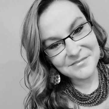 Black and white close-up portrait of a smiling woman wearing glasses and jewelry.