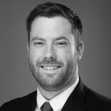 Professional headshot of a smiling man with a beard and green tie.