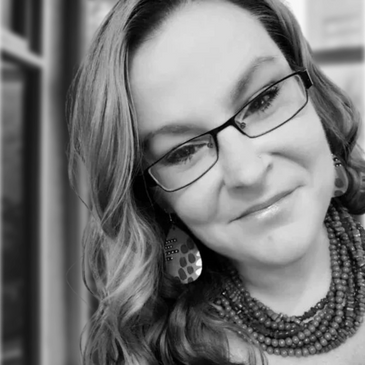 Black and white close-up portrait of a smiling woman wearing glasses and jewelry.