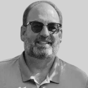 Smiling man with sunglasses and beard in blue shirt.