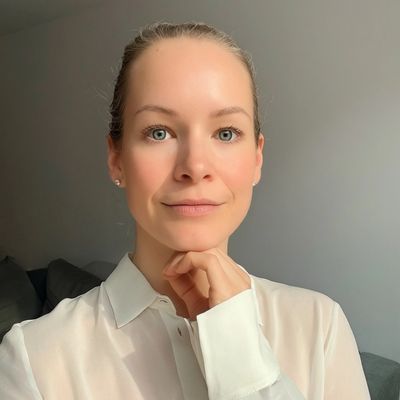 A woman in a white blouse posing with her hand near her chin.