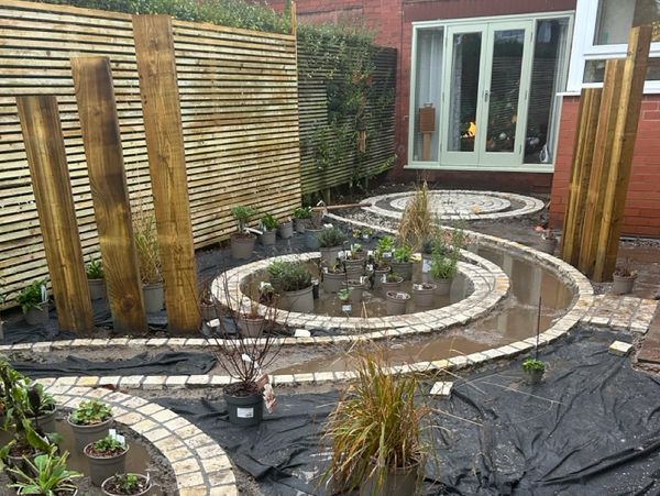 Garden under construction with circular pathways and potted plants.