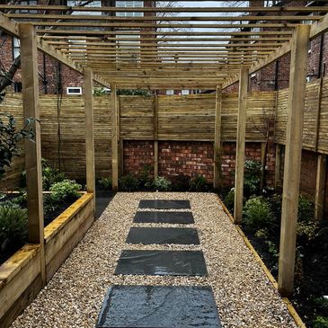 Modern garden pathway with wooden pergola and stone slabs on gravel.