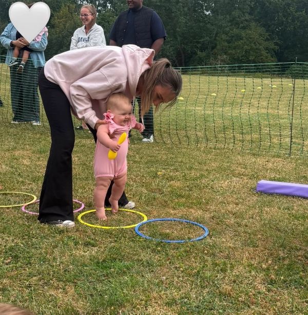Woman helping baby walk on grass with colorful hoops.