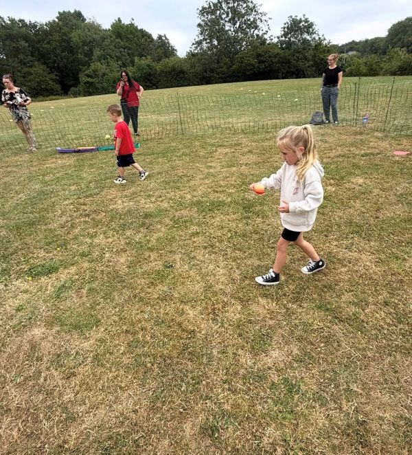 Children playing with balls on a grassy field with adults watching.