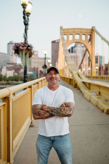 Man with tattoos stands confidently on a yellow bridge in the city.