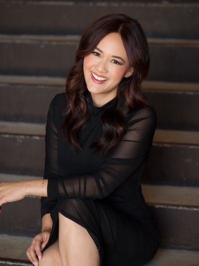 Smiling woman in a black dress sitting on stairs.