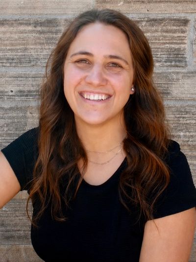 Smiling woman with wavy brown hair against a textured wall.