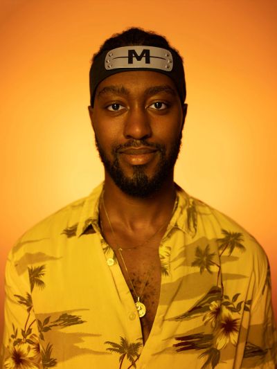 Man wearing a yellow floral shirt and a headband with a letter M.
