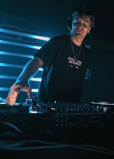 DJ performing in a dimly lit club with vibrant blue lights.