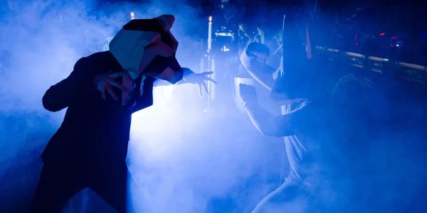 Two figures in animal costumes engage in a dramatic scene with blue fog.