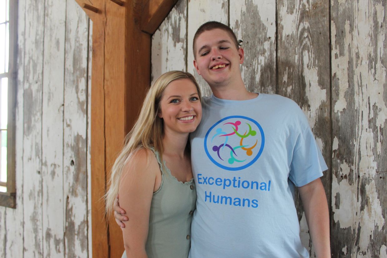Smiling young lady with long blond hair standing beside a smiling young man with a light blue shirt.