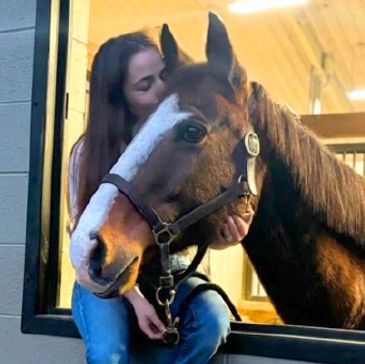 A woman lovingly embraces a horse through a stable window.