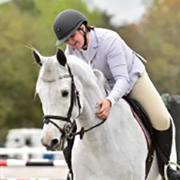 Smiling rider gently pats a white horse during an equestrian event.