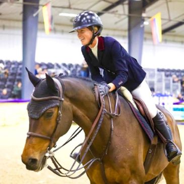 Equestrian rider smiling on a horse inside an arena.