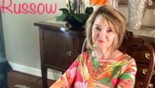 Woman in a colorful dress sitting indoors at a wooden table.
