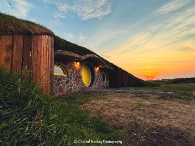 A cozy hobbit-style earth house at sunset with round windows and grassy roof.