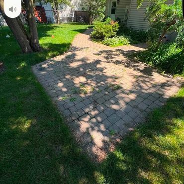 Sunny backyard with a stone patio and green grass.