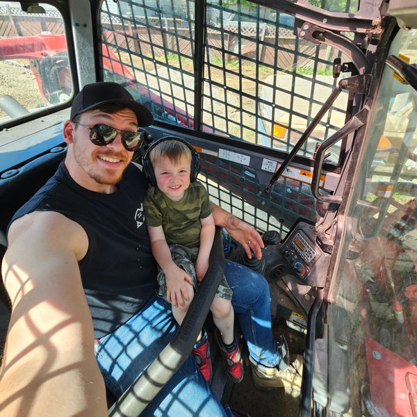 Man and young boy smiling inside construction vehicle cabin.
