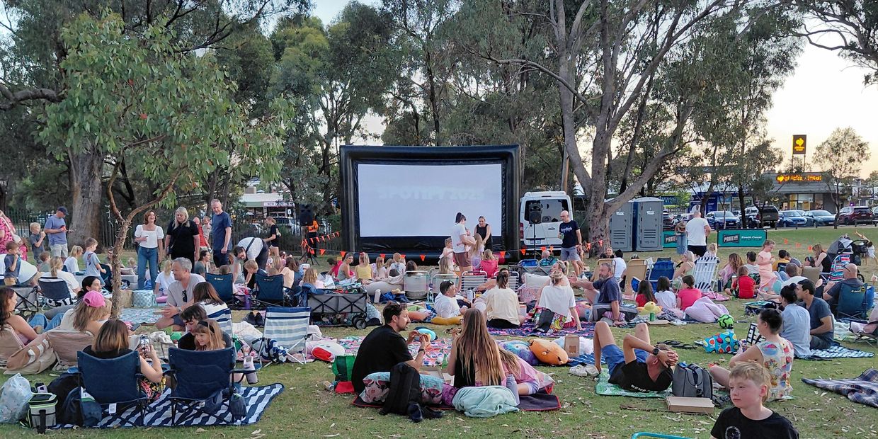 Outdoor movie night with families and friends gathered on blankets and chairs.