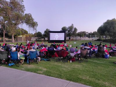 Outdoor movie night with people seated on chairs and blankets.