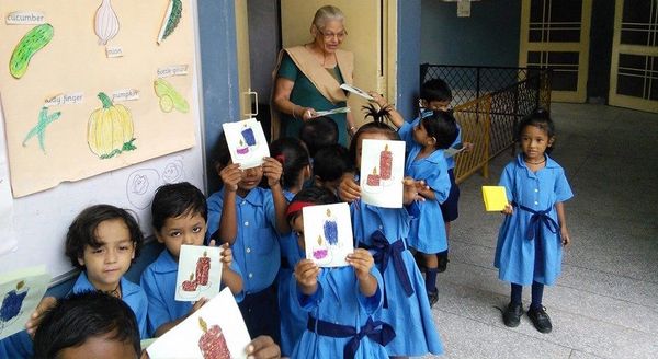 Young children in blue uniforms showing handmade craft cards in a classroom.
