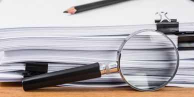 Magnifying glass on stacked documents with pencil and binder clips.