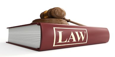 Wooden gavel resting on a thick law book with a maroon cover.