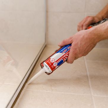 Person applying white silicone sealant along a tiled wall corner.
