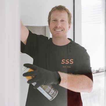 Person cleaning glass with spray and gloves, smiling.