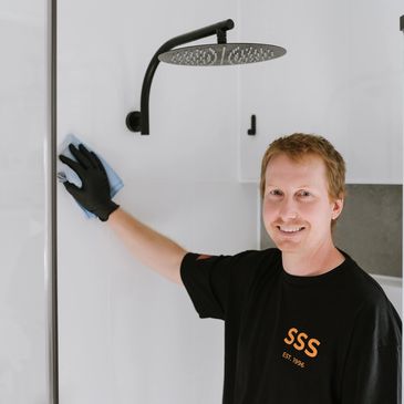 Man cleaning a glass shower wall with a cloth and glove.